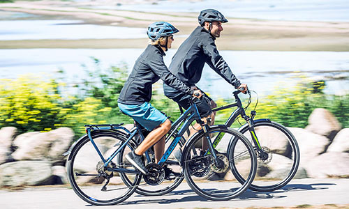 Un uomo e una donna pedalano lungo il mare su biciclette da trekking.