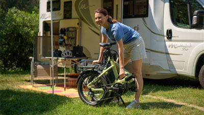 Una donna è in piedi dietro una bicicletta pieghevole verde. Sullo sfondo si vede un camper.