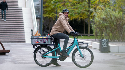 Un ciclista attraversa il centro città con la sua bicicletta blu Cube Longtail. Sul portapacchi ha una cassetta con generi alimentari.