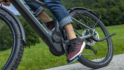 L'immagine mostra un primo piano di una bicicletta ibrida all-road Cube Reaction di colore grigio. Sono in primo piano il movimento centrale e il blocco motore dell'e-bike durante la marcia.