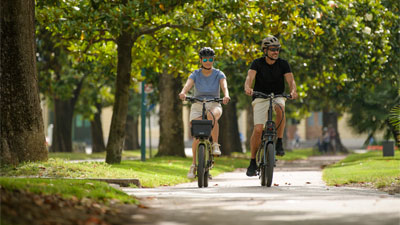 Un uomo e una donna attraversano un parco in sella a biciclette pieghevoli.