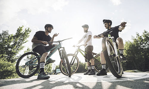 Tre ciclisti freestyle sono in piedi accanto alle loro biciclette e chiacchierano in una giornata di sole.