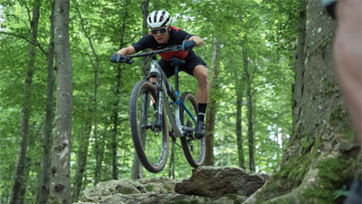 Un ciclista sta attraversando il bosco e sta saltando da una pietra.