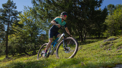Si vede una ciclista sulla sua mountain bike. Sta percorrendo un tratto di strada ripido.