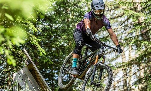 Ciclista con casco integrale in sella a una mountain bike full suspension mentre attraversa il bosco.