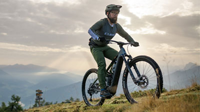 Si vede un uomo su una bicicletta elettrica ibrida Cube Stereo grigia che percorre un sentiero escursionistico.