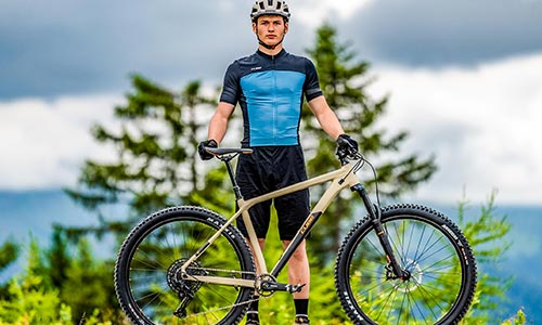 Uomo in abbigliamento da ciclista in piedi dietro una mountain bike hardtail.