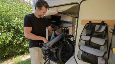 Un uomo ripone la sua bicicletta pieghevole grigia nel suo camper aperto.